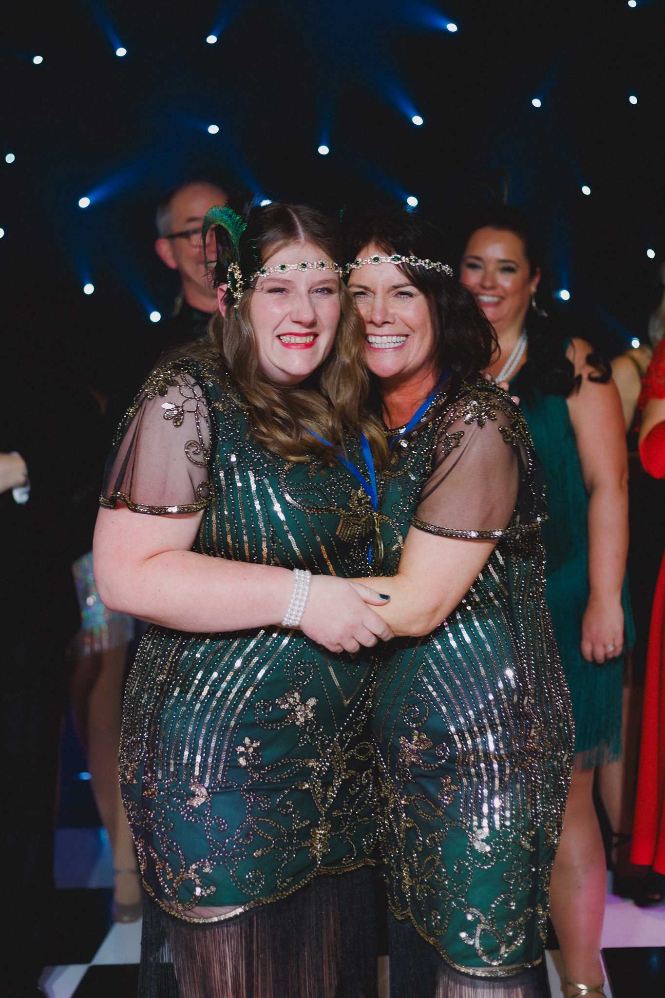 Donna and Helen hugging following the win in green and gold dresses